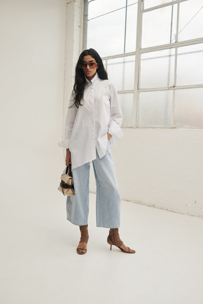 Woman in a white asymmetric button through shirt with light blue wide leg jeans and brown heeled sandals