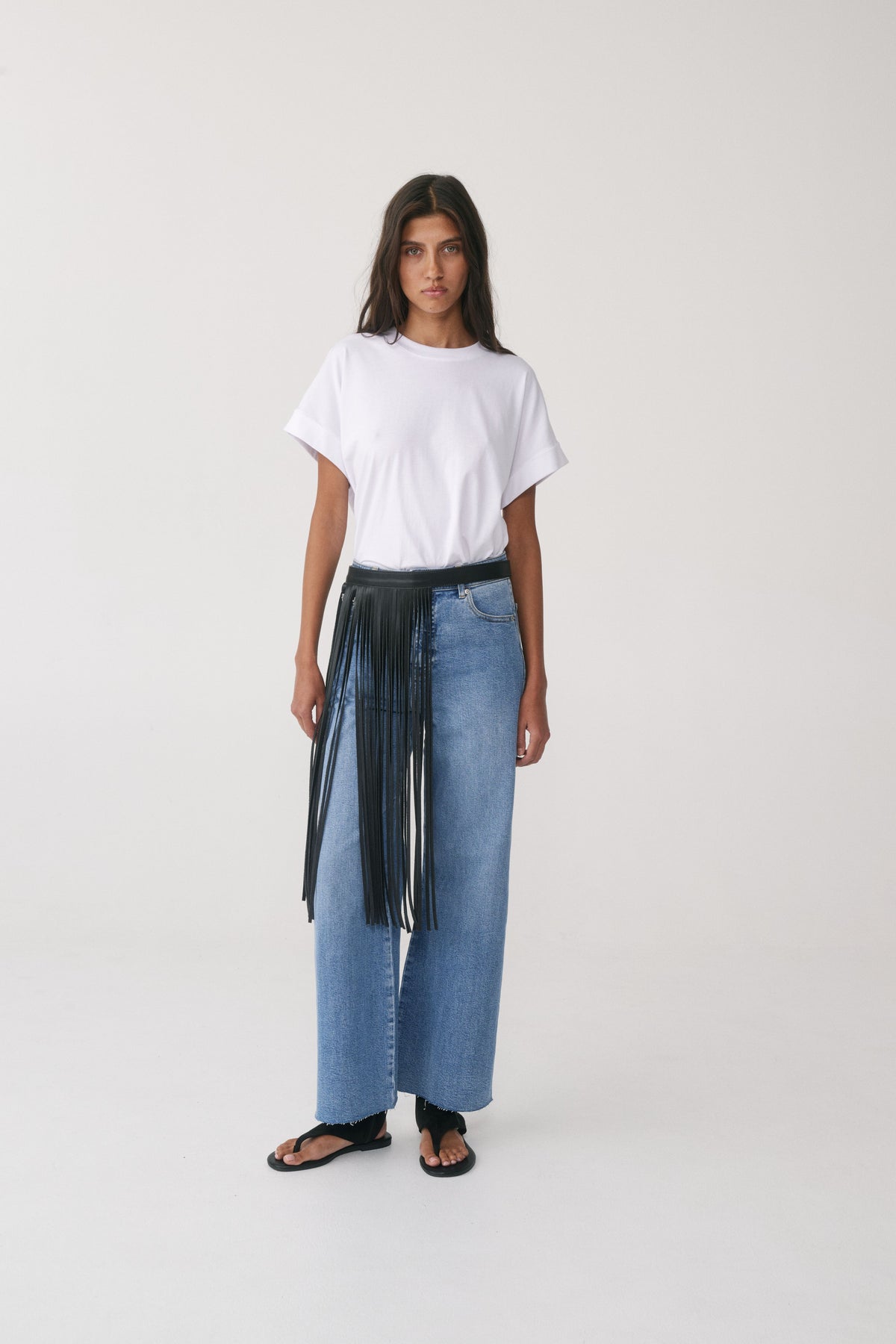 Woman wearing a white tee, blue wide leg jeans and a black leather fringe belt