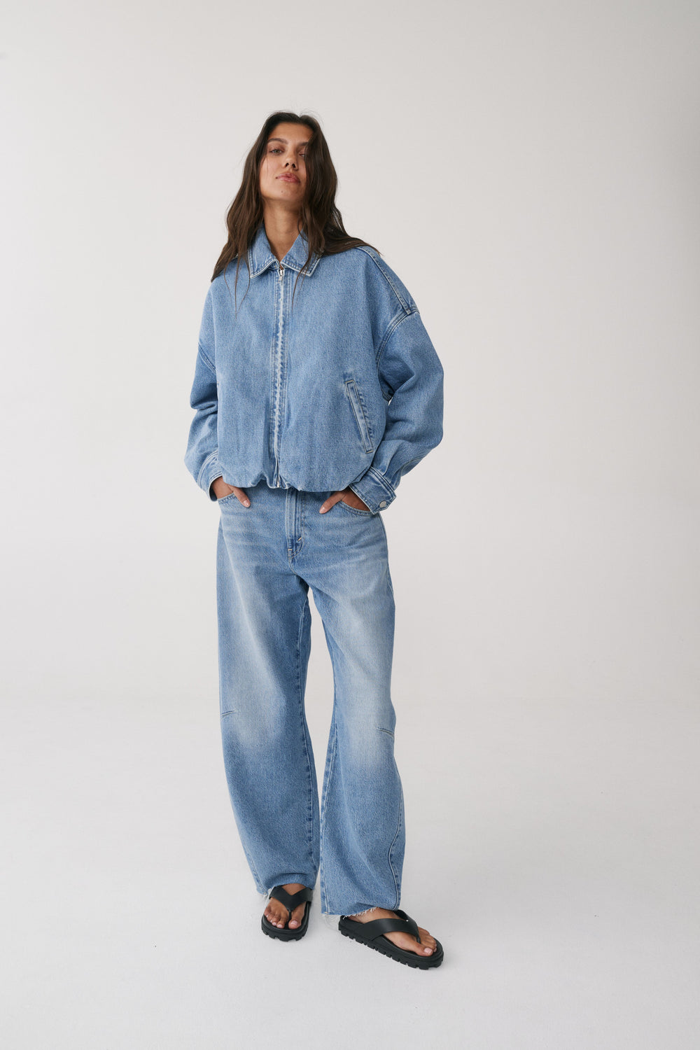 Woman wearing a light blue denim jacket with full length cinched barrel jeans and black sandals