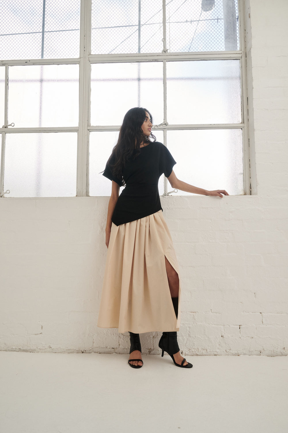 Woman wearing a black and beige spliced pleated midi dress with a side split and black sandals