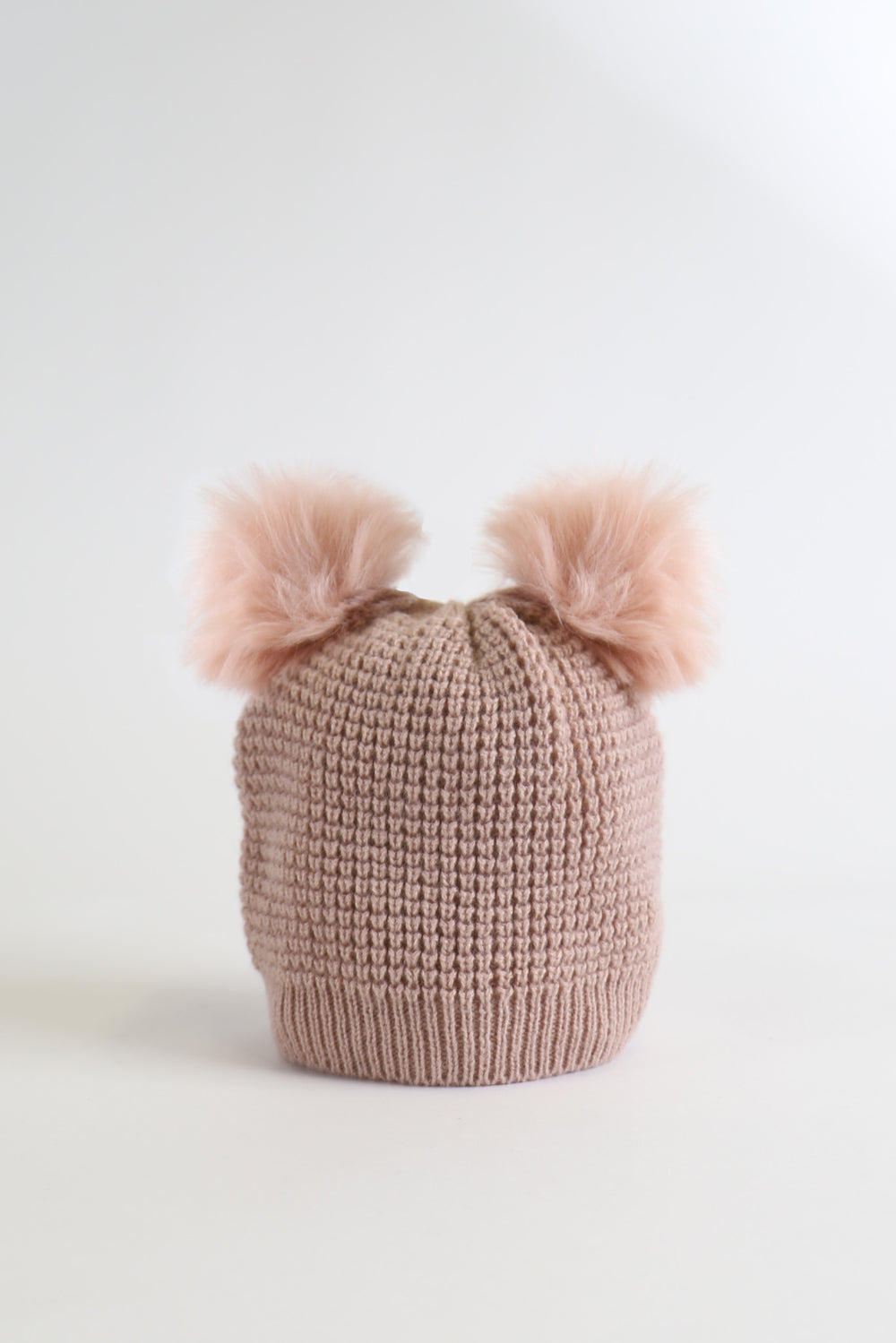 Soft pink knitted girls beanie with two fluffy pom pom details, cozy and stylish winter accessory