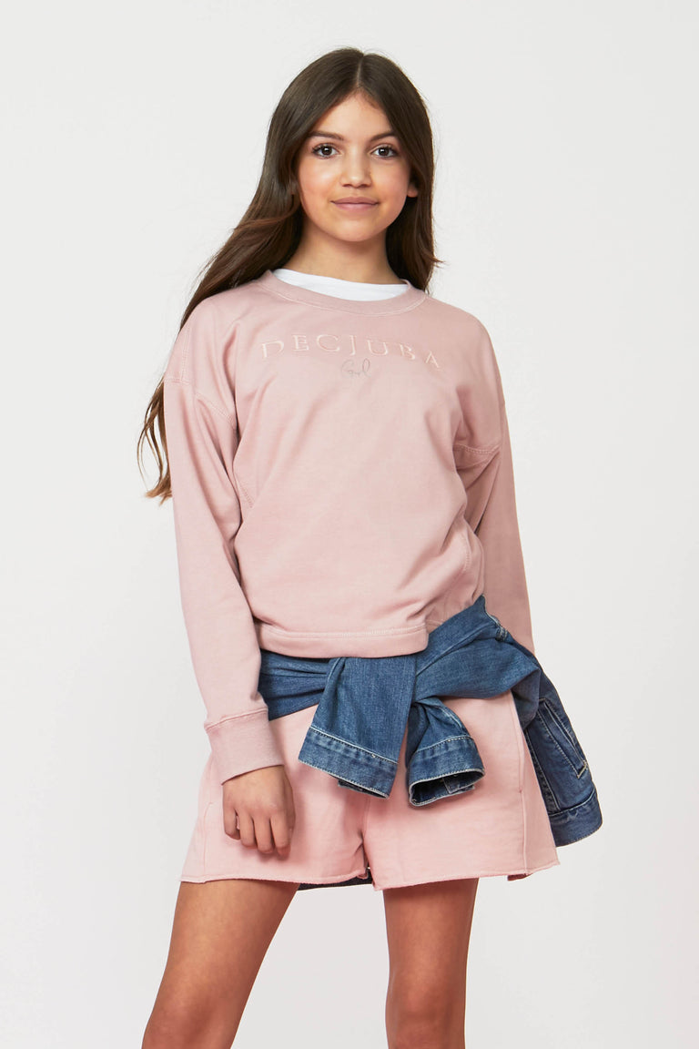Girl wearing a pink crew neck sweatshirt with matching shorts and a denim jacket tied at the waist