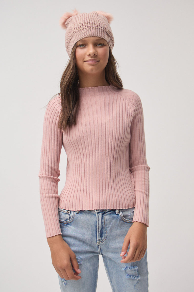 Girl wearing a soft pink ribbed knit top paired with distressed light blue jeans and a blush double pom beanie